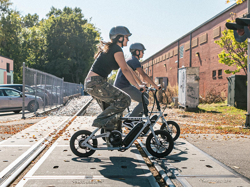 Two people riding the new compact folding electric bike from Schwinn - the Twister - across railroad tracks.